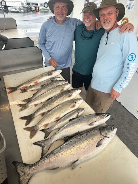 Guests displaying a catch of lake trout and salmon after a successful Traverse City fishing charter on West Grand Traverse Bay