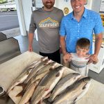 Friends with a young angler showing off a limit of lake trout, a salmon, and a steelhead after a successful Traverse City fishing charter on West Grand Traverse Bay.