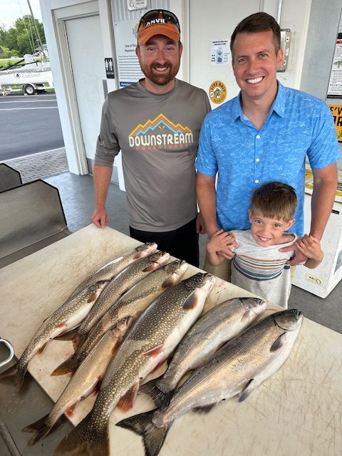 Friends with a young angler showing off a limit of lake trout, a salmon, and a steelhead after a successful Traverse City fishing charter on West Grand Traverse Bay.