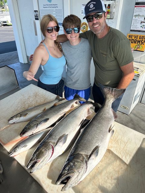 Family showing off four salmon and a lake trout after a successful Traverse City fishing charter on West Grand Traverse Bay.