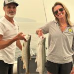 Couple holding a lake trout and steelhead caught during a Traverse City fishing charter on West Grand Traverse Bay