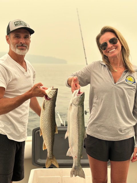 Couple holding a lake trout and steelhead caught during a Traverse City fishing charter on West Grand Traverse Bay