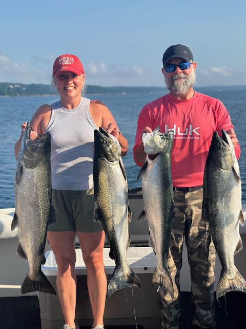 Couple holding four Lake Michigan salmon during a successful Traverse City fishing charter on West Grand Traverse Bay.