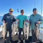 Father and two sons holding king salmon and a lake trout after a successful Traverse City fishing charter on West Grand Traverse Bay.