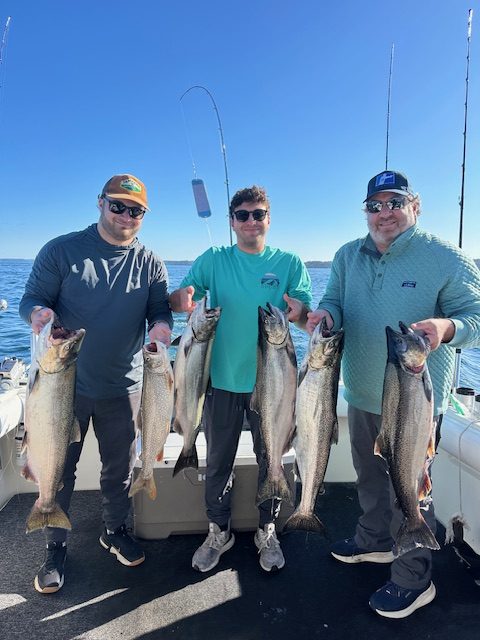 Father and two sons holding king salmon and a lake trout after a successful Traverse City fishing charter on West Grand Traverse Bay.
